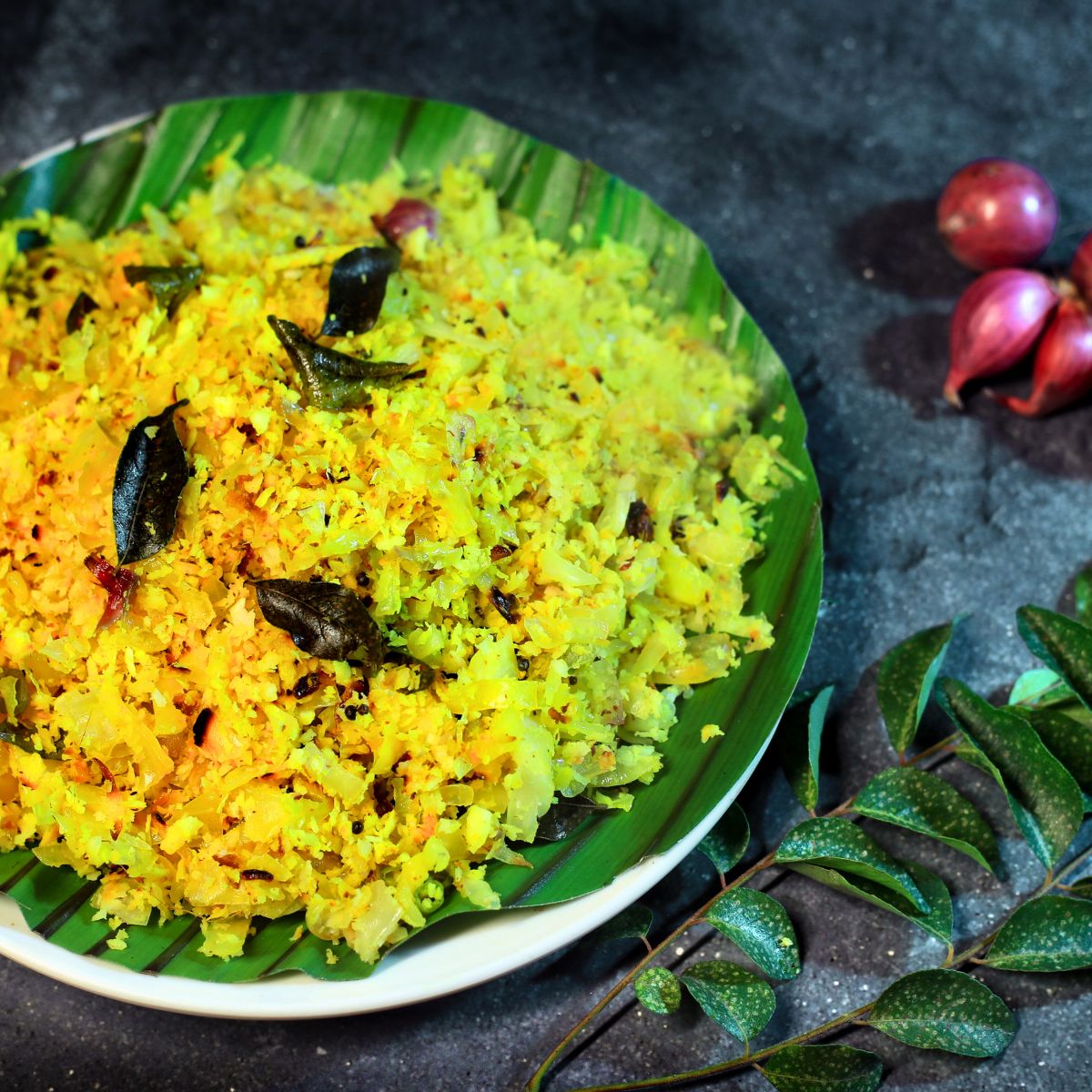 cabbage thoran on a plate with curry leaves and shallots on the side.