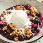 a bowl of blueberry crisp topped with a scoop of vanilla bean ice cream.
