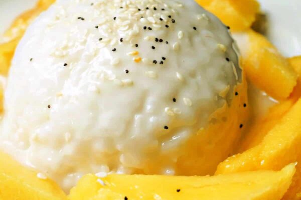 A creamy rice dessert topped with sesame seeds, surrounded by fresh mango slices on a decorative plate.