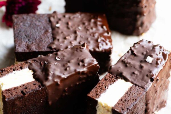 Four chocolate ice cream sandwiches with vanilla ice cream in the middle and dipped in chocolate and hazelnuts on a travertine surface.