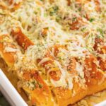 sliced hawaiian roll garlic bread in a white ceramic baking dish. The buns are covered in cheesy garlic butter and chopped herbs.
