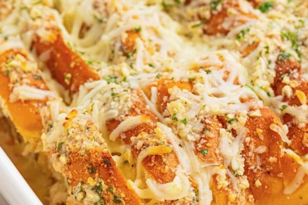 sliced hawaiian roll garlic bread in a white ceramic baking dish. The buns are covered in cheesy garlic butter and chopped herbs.