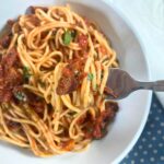 Spaghetti alla puttanesca on a fork lifting from a white plate.