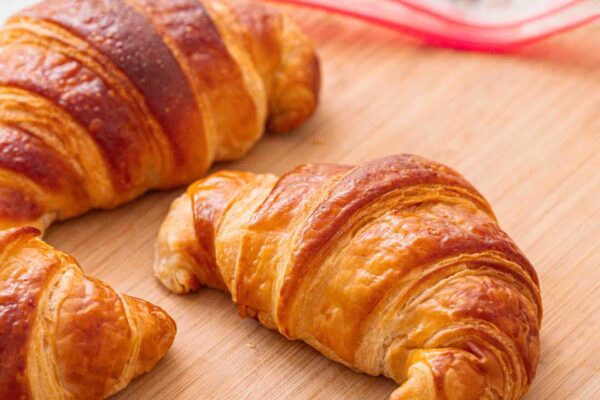 Your Complete Guide to Freezing Croissants Three croissants on a wooden cutting board, with a black marker and a zipped plastic bag in the background.
