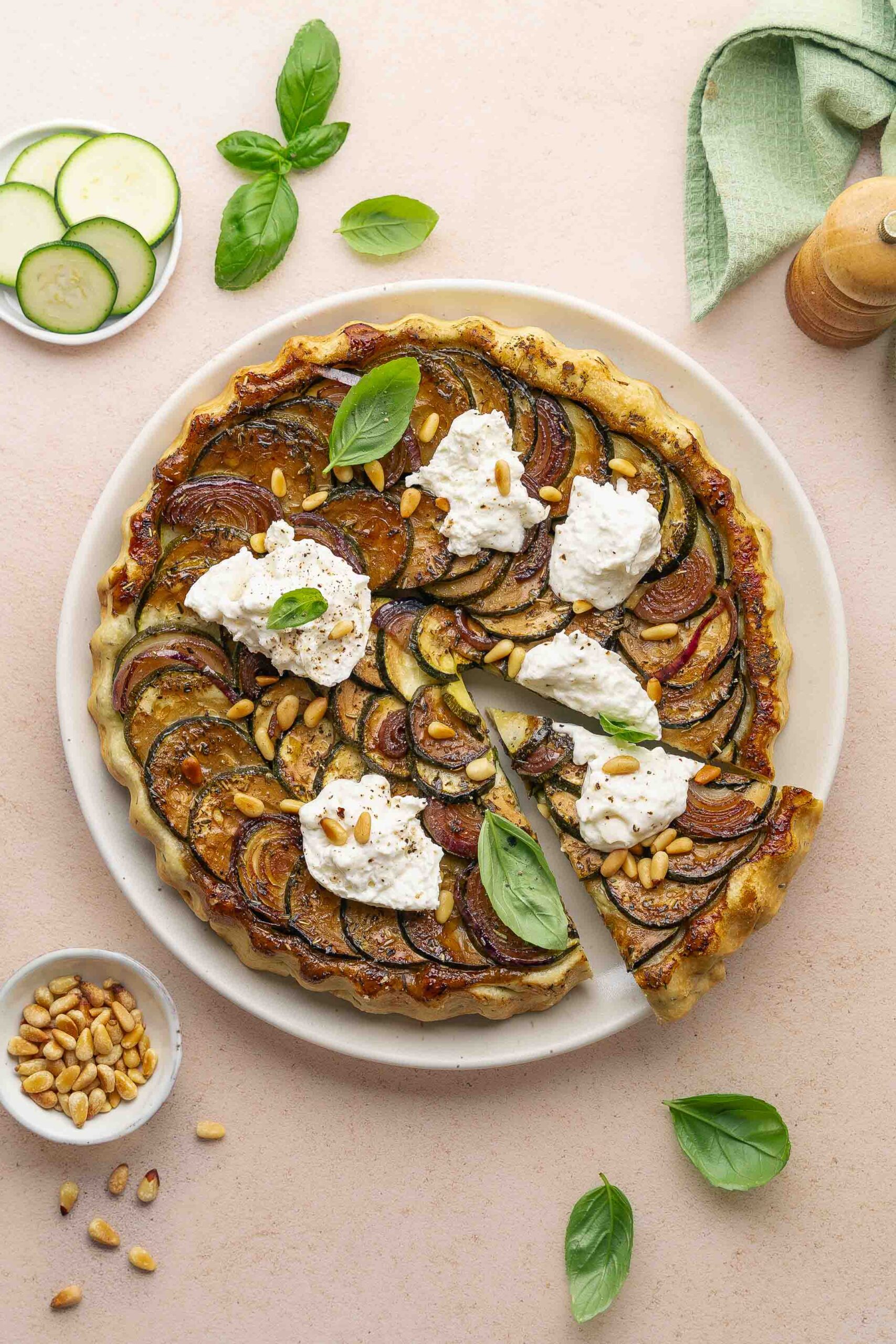 Zucchini Tarte Tatin (Easy & Quick) 1 Zucchini tarte tatin topped with creamy burrata, toasted pine nuts, and fresh basil leaves, served on a round white plate with a slice cut out.