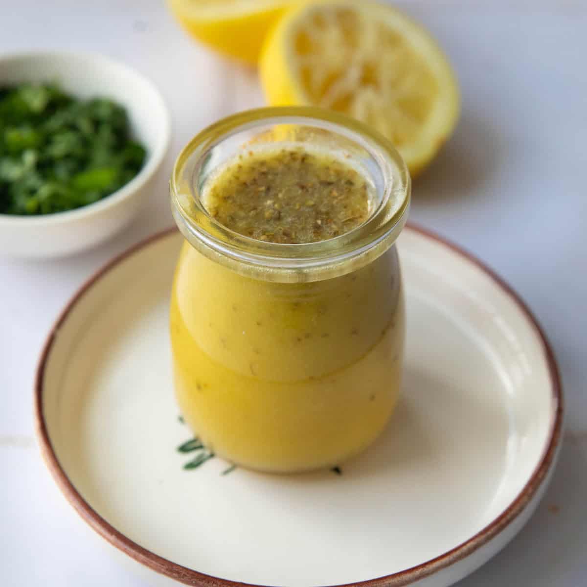 Mediterranean Salad Dressing (5 Minutes!) • Unicorns within the Kitchen 1 a shot of a mason jar with Mediterranean salad dressing placed on a plate