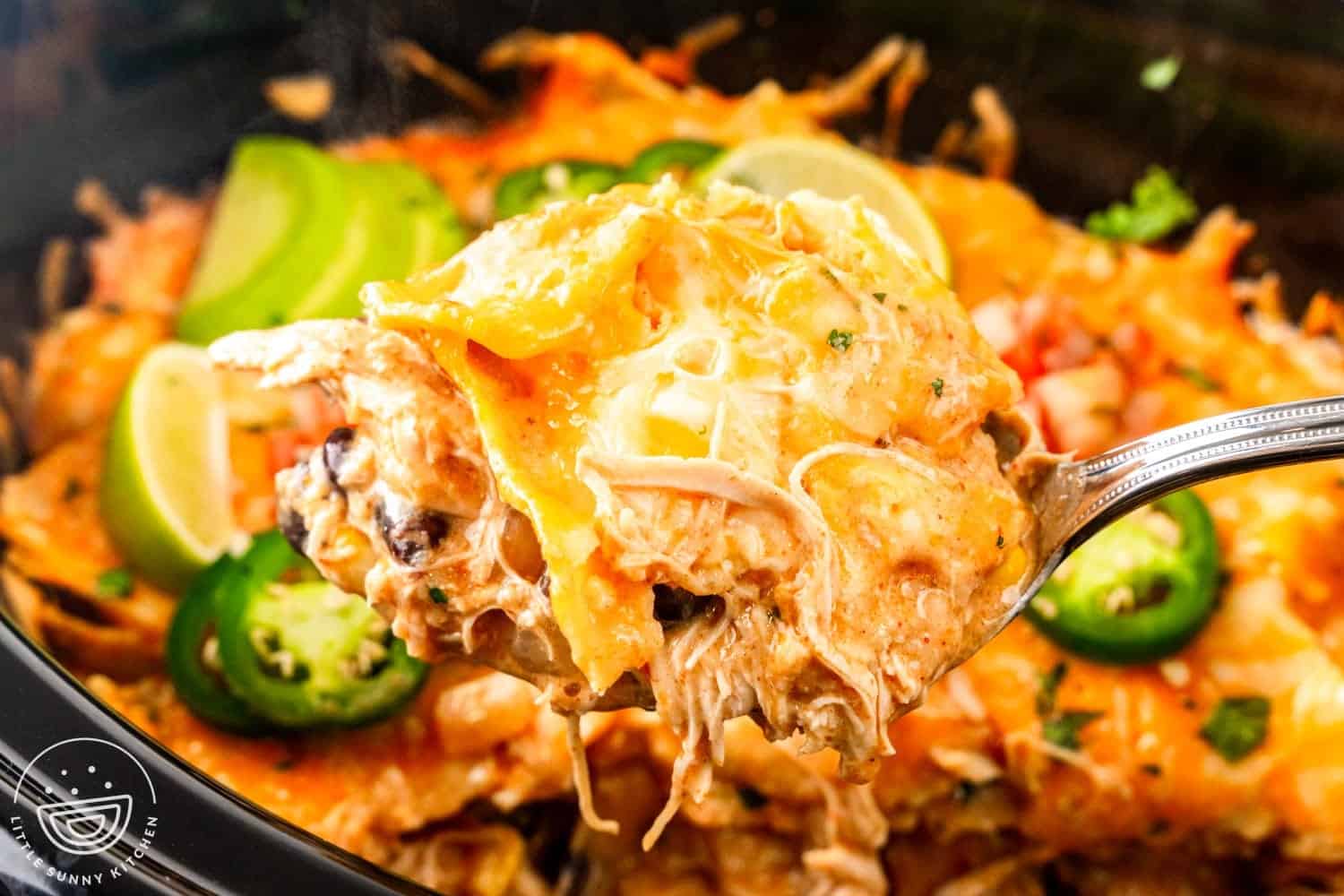 closeup of a scoop of enchilada casserole with shredded chicken topped with tortillas and cheese.