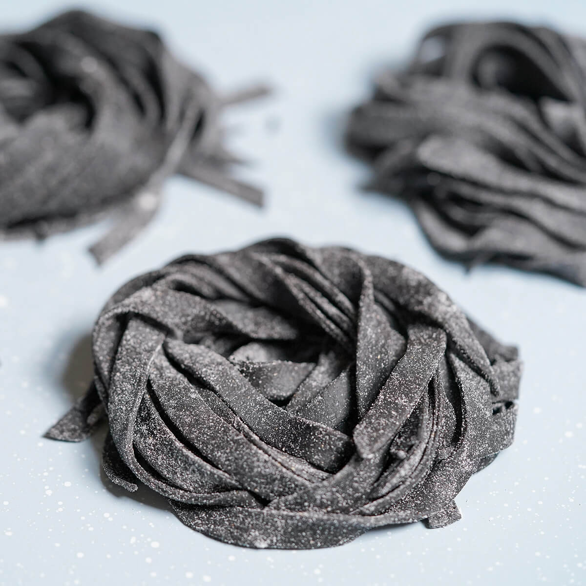 Homemade squid ink pasta - Caroline's Cooking 1 small stack of squid ink pasta on tray with others blurred behind.