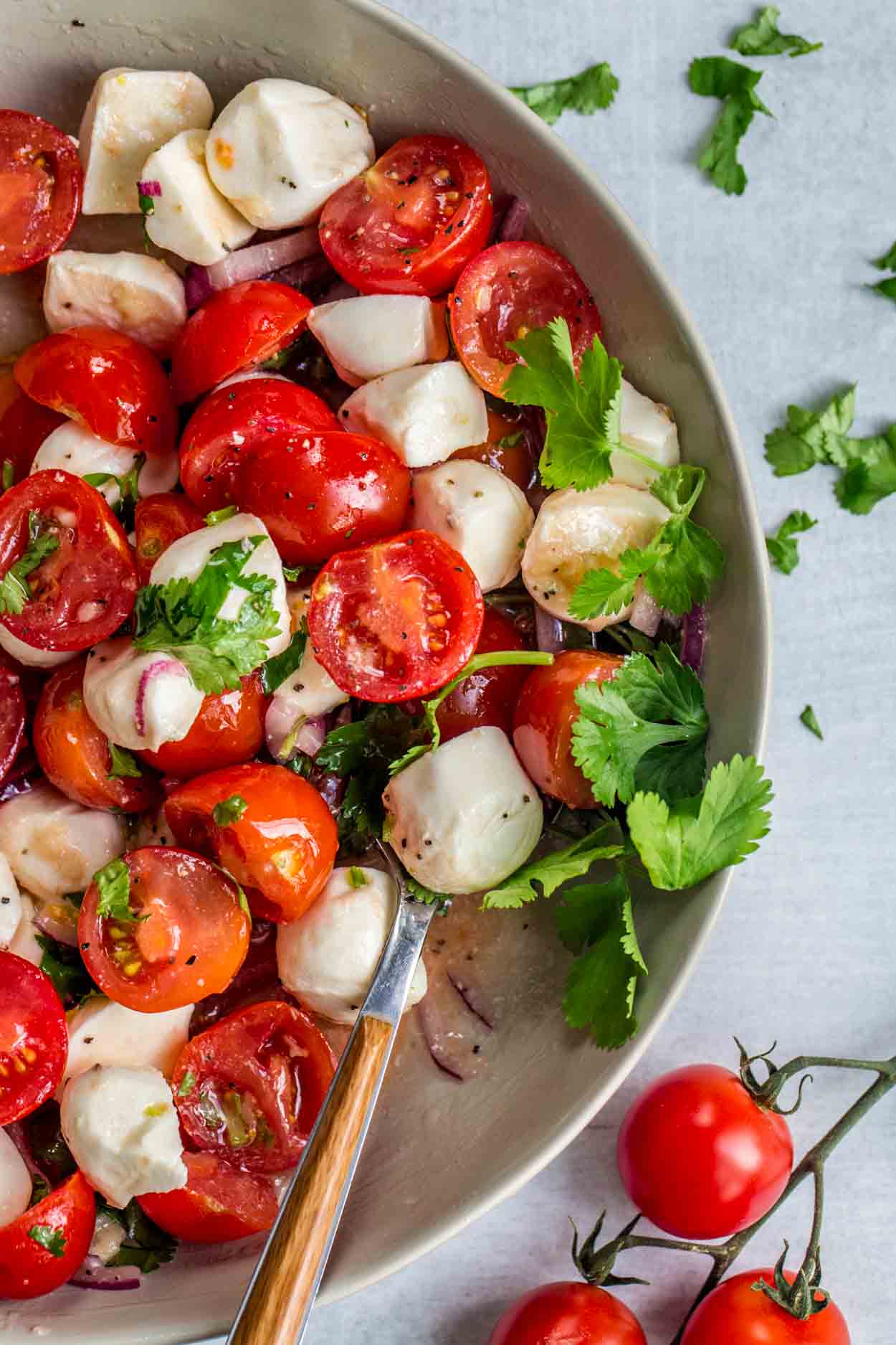 Tomato Mozzarella Salad Recipe - Valentina's Corner 1 Tomato mozzarella salad in a gray plate with a spoon and fresh greens.